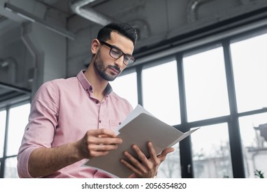 Low Angle View Of Muslim Businessman In Eyeglasses Looking At Paper Folder In Office