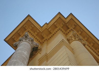 Low angle view of a neoclassical building facade showing prominent roof cornice molding supported by decorative pillars against clear blue sky.