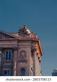Low Angle View of Neoclassical Building Corner with Corinthian Columns and Allegorical Sculpture Against Deep Blue Sky, Paris, France
