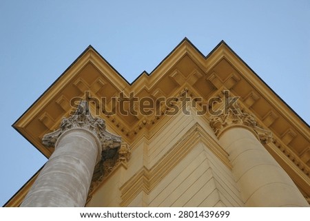 Low angle view of a neoclassical building facade showing prominent roof cornice molding supported by decorative pillars against clear blue sky.
