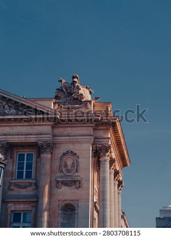 Low Angle View of Neoclassical Building Corner with Corinthian Columns and Allegorical Sculpture Against Deep Blue Sky, Paris, France