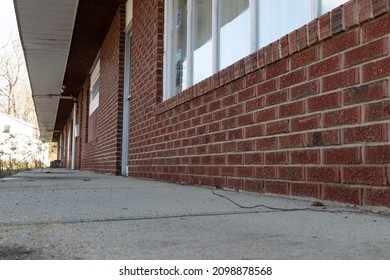 A Low Angle View Of An Old Abandoned Strip Mall With Several Red Brick Store Fronts Closed After Long Struggle To Maintain Business.