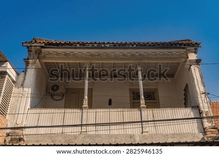 Low angle view of an old classic colonial heritage architecture building facade featuring a vintage balcony, wooden pillars, and clear blue sky in Gresik old town.