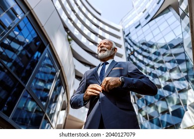 Low angle view of an old successful bearded businessman buttoning his vest while standing at the business center. It is very important who is your leader, and, if you can choose- choose the best.