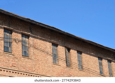 A low angle view of an old weathered brick factory building with many tall windows under a clear blue sky
