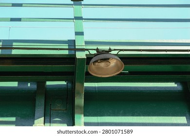 Low angle view of an old weathered industrial light fixture with a visible bulb attached to a green painted steel beam construction.