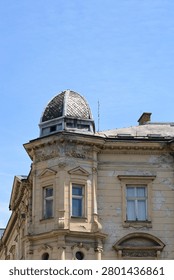 Low angle view of an old weathered building corner with a decorative tiled dome top and damaged plaster facade under a clear blue sky.