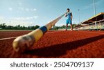 Low angle view on male pole vault athlete in blue uniform standing at open air stadium with pole, getting ready for endurance training. Concept of sport, championship, tournament, active lifestyle