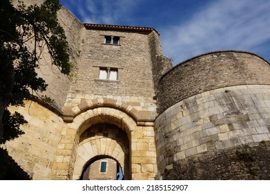 Low angle view on a massive, stone castle, featuring round towers, old mullion windows and a fortified gate formerly equipped with a harrow, in Cordes-sur-Ciel, a medieval village in Southern France