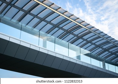 Low angle view on a modern glass and steel skybridge, with a cloudy blue sky background