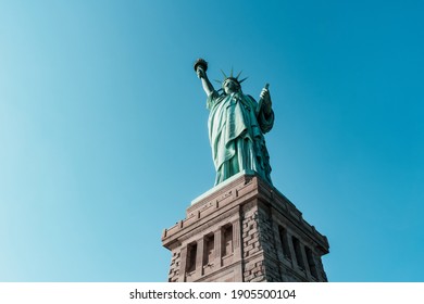 Low angle view on Statue of Liberty National Monument, New York, USA. Famous colossal copper sculpture standing on stone pedestal know as world symbol of freedom. View against blue cloudless sky. - Powered by Shutterstock