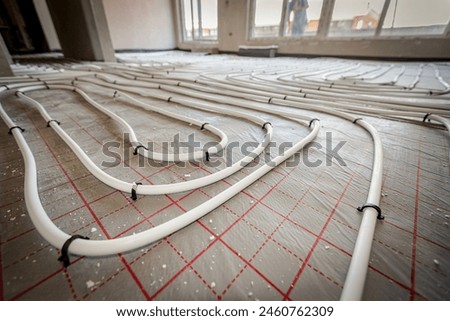 Low angle view on thin white tubes bended in complex curve of new brass distribution system manifold mounted for central heating floor in a residential building under construction.