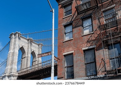 Low angle view of one of the suspension towers of the Brooklyn Bridge in New York City, NY, USA with iconic, historic brick buildings on Old Fulton Street in foreground