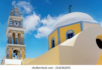Low angle view of one of the typical yellow church buildings with colorful clock and bell tower on Santorini, Greece, against a white clouded blue sky