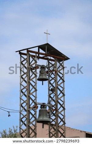 Low angle view of an open metal frame church bell tower with two bronze bells against blue sky