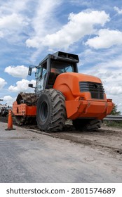 Low angle view of an orange single-drum padfoot soil compactor roller on a road construction site.