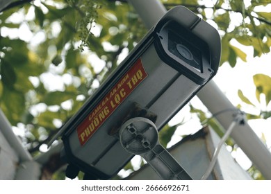 Low angle view of an outdoor security camera mounted on a pole. CCTV surveillance system for public safety with a blurred green background.