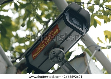 Low angle view of an outdoor security camera mounted on a pole. CCTV surveillance system for public safety with a blurred green background.