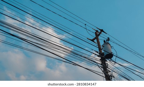 Low angle view of overhead utility cables and power lines crossing a clear blue sky with soft clouds, representing urban electricity and communication networks