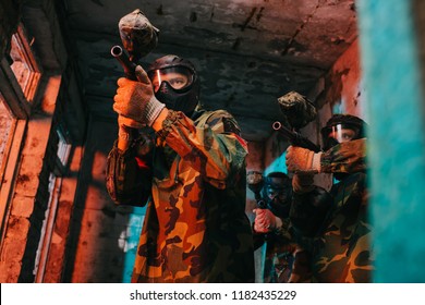 low angle view of paintball team in uniform and protective masks aiming by paintball guns in abandoned building