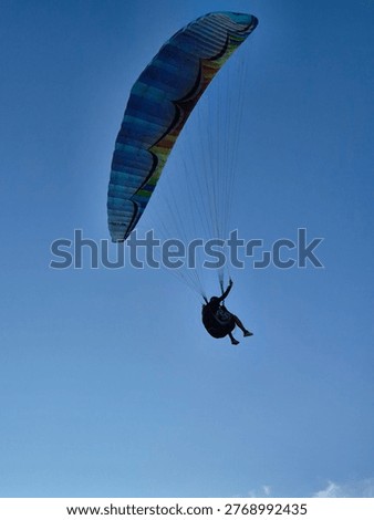 Low angle view of paraglider in flight against clear blue sky, highlighting movement and freedom.