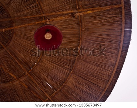 Low angle view of a parasol with red lamp in straw wicker pattern of lines and bright sky