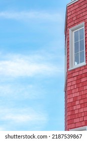 Low angle view of a part of a house with red wooden shingles in San Francisco, California. Bay window of a house with picture window with white frames and a view of a sky on the side.