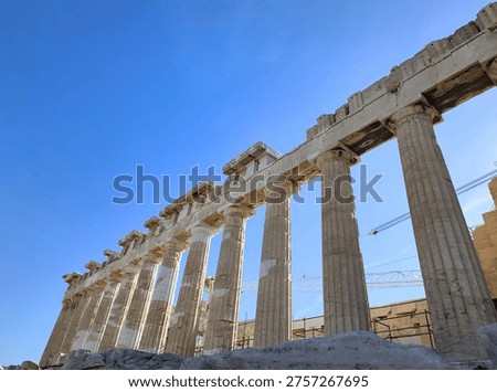 Low angle view of the Parthenon's Doric columns and architrave under restoration at the Acropolis of Athens, Greece. The ancient marble temple with a construction crane against a blue sky.