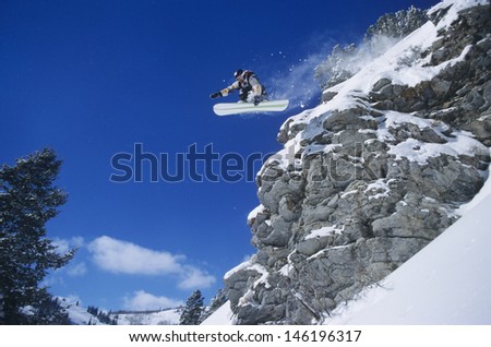 Low angle view of a person on snowboard jumping midair over cliff