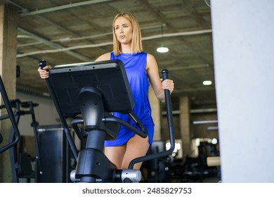 Low angle view photo of a blonde young fit caucasian woman exercising on elliptical machine - Powered by Shutterstock