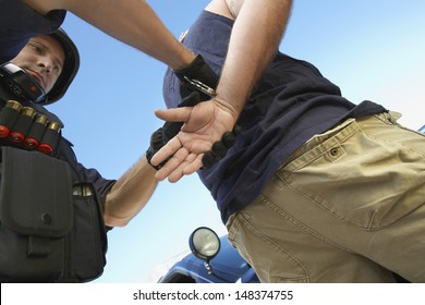 Low angle view of policeman arresting criminal against sky