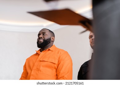 Low Angle View Of Positive African American Man In Jail Uniform Near Guard In Court On Blurred Foreground