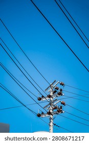 Low angle view of a power distribution pole with multiple electrical wires and ceramic insulators against a clear blue sky