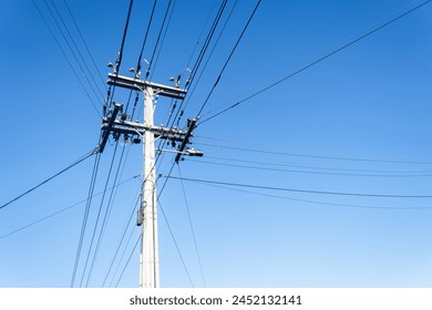 Low angle view of power post and powerlines against a cloudless blue sky. Auckland. 