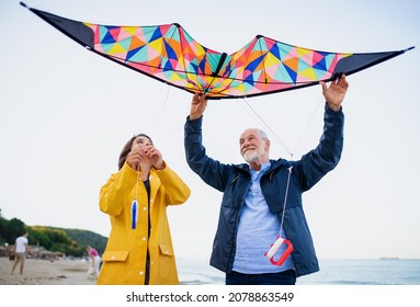 Low angle view of preteen girl and her grandfather playing with kite on sandy beach.