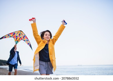 Low angle view of preteen girl and her grandfather playing with kite on sandy beach.