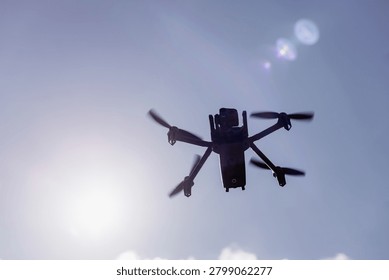 Low angle view of a professional quadcopter drone with rotating propellers flying high in the clear blue sky