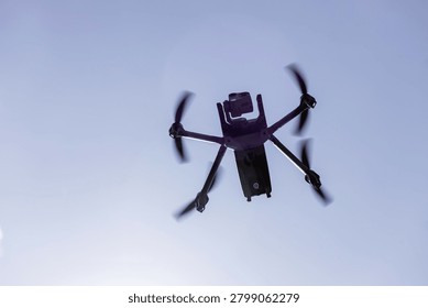 Low angle view of a professional quadcopter drone with rotating propellers flying high in the clear blue sky