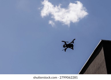 Low angle view of a professional quadcopter drone with rotating propellers flying high in the clear blue sky