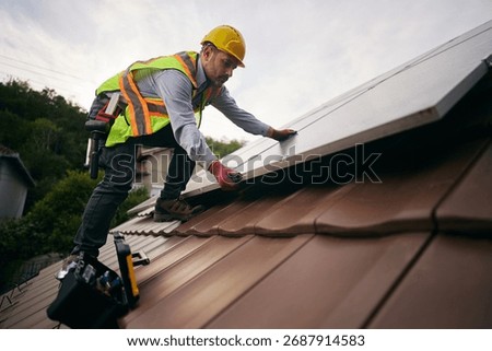 Low angle view of professional worker covering roof with solar panels. Copy space.