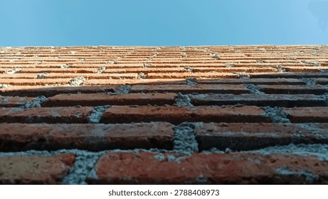Low angle view of a red brick wall against clear blue sky. Detailed texture of rustic bricks with perspective composition creating an abstract architectural background. Perfect for construction, urban design, exterior building texture, minimalist wallpaper, and modern architecture concepts.”