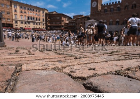 Low angle view of the red brick pavement of Piazza del Campo in Siena, Italy, with a crowd gathering before the historic Palio horse race.