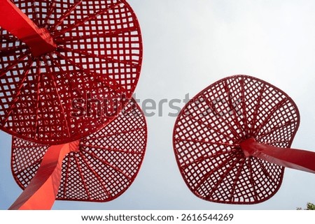 Low angle view of red perforated metal discs against white sky, abstract industrial design.