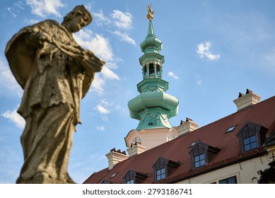 Low angle view of a religious stone sculpture with the Franciscan Church clock tower, Old Town, Bratislava, Slovakia, Central Europe.