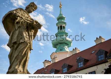 Low angle view of a religious stone sculpture with the Franciscan Church clock tower, Old Town, Bratislava, Slovakia, Central Europe.