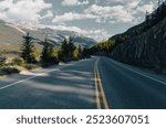 low angle view of a road with two yellow lines vanishing into the mountains on a sunny day in the shadow