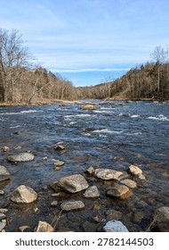 Low angle view of rushing river rapids and bare forest under clear blue sky