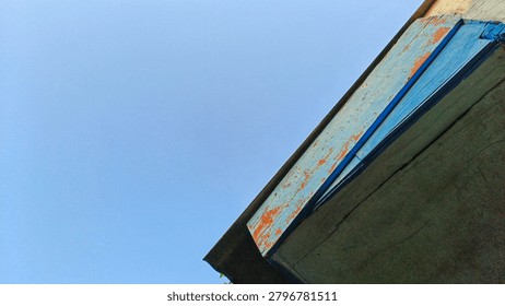 Low angle view of a rustic building roof corner against a clear blue sky