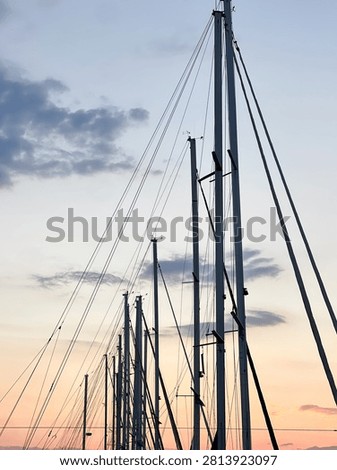 Low angle view of sailboat masts and rigging against a beautiful twilight sky, silhouettes of yacht masts at a marine harbor port during sunset with soft colorful clouds.