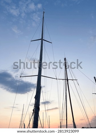 Low angle view of sailboat masts and rigging against a beautiful twilight sky, silhouettes of yacht masts at a marine harbor port during sunset with soft colorful clouds.